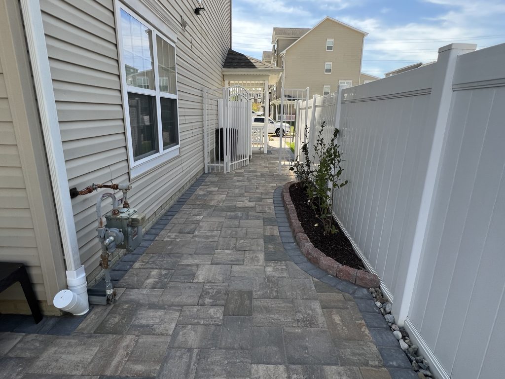 Stone patio to side of house with white fence bordering